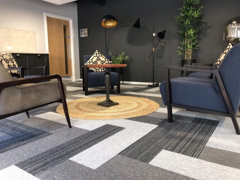 Photo of a small seating area with several armchairs around a table. The photo is highlighting the tiled carpet flooring.